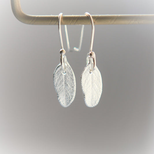 Earrings in the shape of a small sage leaf approximately 15mm long and 7mm wide made of pure silver. They have the texture and shape of a real sage leaf. Each earring has a small hole at the top where the sterling silver ear wire attaches. The ear wires are hand made and come with a complimentary plastic safety stopper that prevents loss.