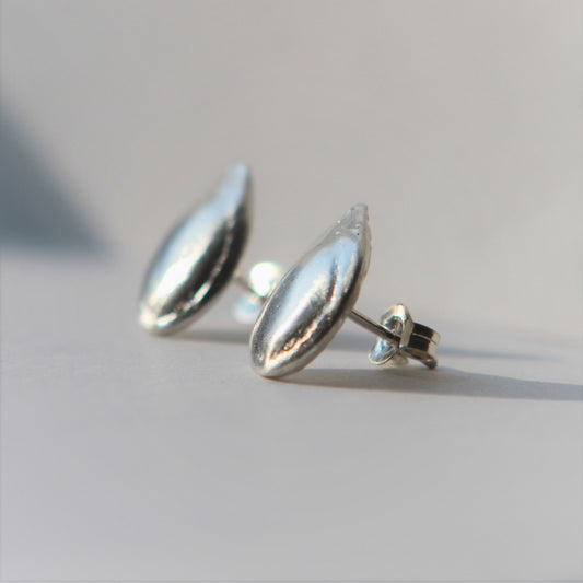 Stud Earrings in the shape of a small pumpkin seed approximately 13 mm long by 8 mm wide made of pure silver.  Each earring has sterling silver ear posts and butterfly backs.