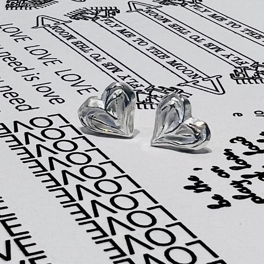 Stud Earrings in the shape of a heart. The shape is formed from a tiny hand carved mould with fine lines resembling those of a peace sign. Each earring is approximately 7mm wide and high and is made of pure silver. Each earring has sterling silver ear posts and butterfly backs.