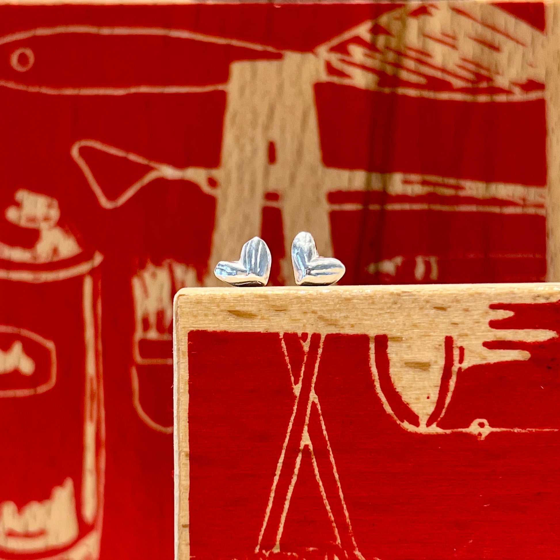 Stud Earrings in the shape of a heart.  The shape is formed from a tiny hand carved mould that has a slight carving texture however the overall look and feel is quite simple and smooth.  Each earring is approximately 6mm wide and high and is made of pure silver.  Each earring has sterling silver ear posts and butterfly backs.